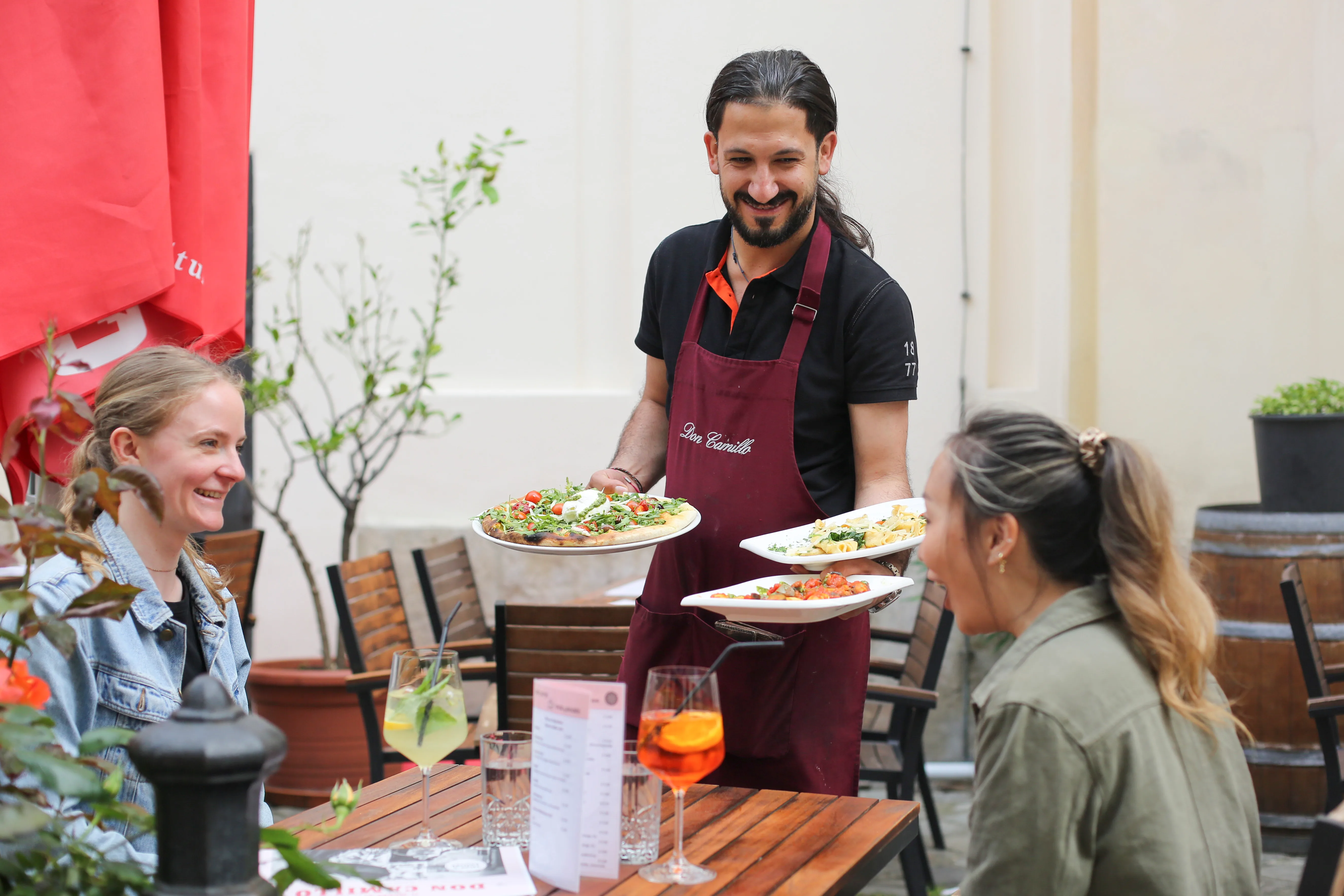 Gäste im Gastgarten der Brückengasse, Pizza und Pasta werden serviert